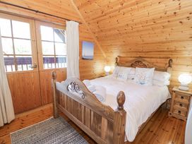 A wooden bedroom with a double bed two bedside tables lamps and a door to a balcony at Sun View Lodge in Llanbedr