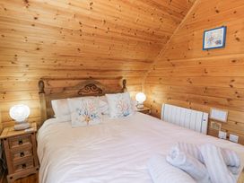 A bedroom with a wooden bed frame white bedding two bedside tables with lamps and wooden walls at Sun View Lodge in Llanbedr