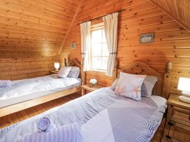 A wooden bedroom with two single beds bedside tables and a window with curtains at Sun View Lodge in Llanbedr
