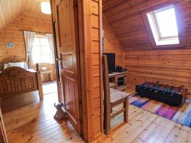 A wooden cabin interior with a bed and window in one room and a foosball table and television in another at Sun View Lodge Llanbedr