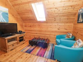 A wooden room with a television on a cabinet a foosball table two blue chairs and a skylight window at Sun View Lodge in Llanbedr