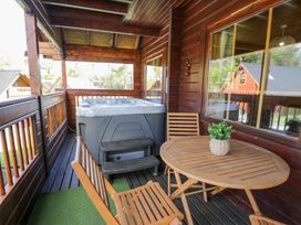 A covered wooden balcony with a hot tub table with a plant and wooden chairs at Sun View Lodge in Llanbedr