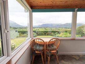 A conservatory with a table and chairs overlooking a garden at Squirrel Cottage in Bassenthwaite