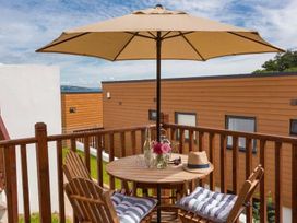 A balcony with a round wooden table and two chairs under a large umbrella at Egret in Brixham