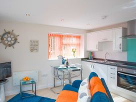 A kitchen with white cabinets and glass dining table next to a blue and orange sofa at Egret in Brixham