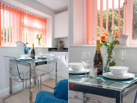 A dining area with a glass table set for two with clear chairs orange vertical blinds and flowers at Egret in Brixham