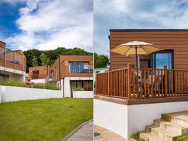 Modern wooden lodges with glass balconies and a patio with a wooden railing and umbrella at Egret in Brixham