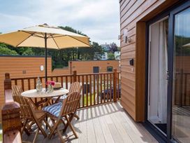 A wooden balcony with table chairs umbrella and flowers outside a house at Egret in Brixham