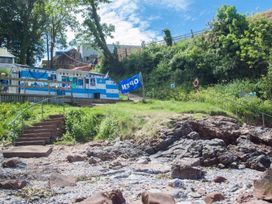 A rocky shoreline with stone steps leading up to a blue and white building with an open flag at Egret in Brixham