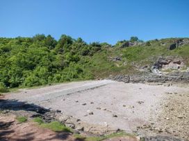 A rocky beach with green shrubs and trees on nearby hills under a clear blue sky at Egret in Brixham
