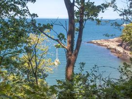 A coastal view through trees with a sailboat on the water and rocky shoreline at Egret in Brixham