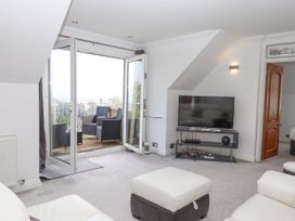 A living room with a television on a stand and a door leading to a balcony with outdoor chairs at Flat 3 Channel View in Torquay