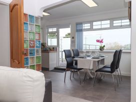 A dining area with a table set for four and black chairs next to large windows and a small kitchen in Flat 3 Channel View Torquay