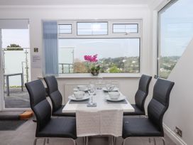 A dining area with a table set for six and black chairs by large windows at Flat 3 Channel View in Torquay
