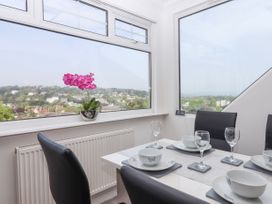 A dining area with a table set with bowls, plates, and wine glasses by large windows overlooking a town and greenery at Flat 3 Channel View in Torquay