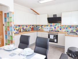 A kitchen with white cabinets colorful tiled backsplash and a dining table with black chairs at Flat 3 Channel View in Torquay