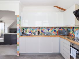 A kitchen with white cabinets colorful tiled backsplash and appliances including toaster kettle and microwave at Flat 3 Channel View in Torquay