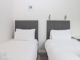 A bedroom with two single beds with gray headboards white bedding and wall-mounted reading lights at Flat 3 Channel View in Torquay