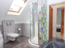A bathroom with a wall-mounted toilet a corner shower with a glass door a skylight and colorful glass tiles beside the shower at Flat 3 Channel View in Torquay