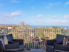 A balcony with four chairs and a table overlooking trees rooftops and the sea at Flat 3 Channel View in Torquay