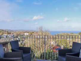 A balcony with four black chairs and a metal railing overlooking trees houses hills and the sea at Flat 3 Channel View in Torquay