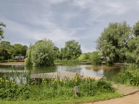 A pond with trees and a dock at Oak Lodge At Bridge Lake Farm & Fishery Chacombe