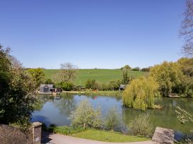 A view of a lake with greenery and a building at Oak Lodge At Bridge Lake Farm & Fishery Chacombe