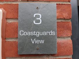 A gray plaque with the number 3 and the words Coastguards View mounted on a red brick wall at Coastguards View Whitby