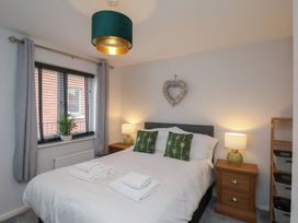 A bedroom with a bed with green patterned pillows two bedside tables with lamps and a window with gray curtains at Coastguards View in Whitby