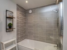 A bathroom with a bathtub and gray tiled walls with a wall shelf holding a plant and a decoration at Coastguards View in Whitby