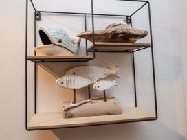 A black metal wall shelf with wooden surfaces holding a ceramic whale, a driftwood piece, and three white wooden fish on stands