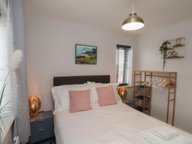 A bedroom with a bed pink pillows bedside tables with lamps a wooden clothes rack and a painting on the wall at Coastguards View in Whitby