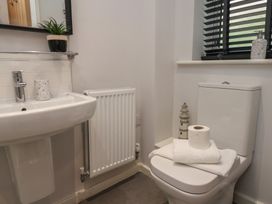 A bathroom with a white sink, radiator, toilet with towels and toilet paper, a small lighthouse decoration, plants on a shelf and window blinds at Coastguards View in Whitby