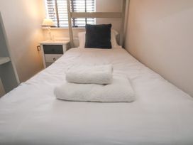 A bedroom with a single bed with white bedding and two folded white towels a small bedside table with a lamp and a window with blinds at Coastguards View in Whitby