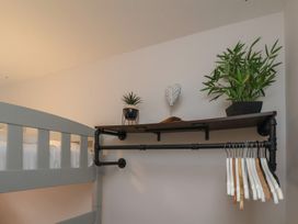 A gray bunk bed next to a wall mounted shelf with plants and a decorative item and hangers hanging from a pipe