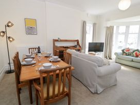 A dining area with a wooden table set for six next to a living room with sofas and a television at Seawinds 2a in Rhos-On-Sea