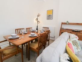 A dining table set for six with wooden chairs and a sofa with colorful cushions in a living room at Seawinds 2a in Rhos-On-Sea