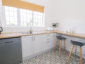 A kitchen with a wooden countertop white cabinets a sink a toaster a plant two stools and patterned floor at Seawinds 2a in Rhos-On-Sea