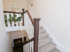 A staircase with carpeted steps and wooden bannisters with white panels and a plant on the landing at Seawinds 2a in Rhos-On-Sea