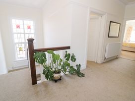 A hallway with a carpet floor a potted plant near a wooden stair railing a stained glass window and doorways leading to other rooms at Seawinds 2a in Rhos-On-Sea