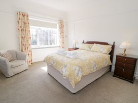 A bedroom with a bed with yellow floral bedding two bedside tables with lamps a window with floral curtains and an armchair at Seawinds 2a in Rhos-On-Sea