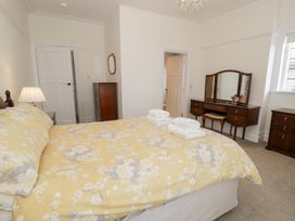 A bedroom with a yellow floral bedspread wooden dressers a vanity and a window at Seawinds 2a in Rhos-On-Sea