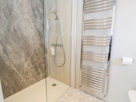 A shower area with a glass panel and a handheld showerhead next to a chrome towel radiator and toilet paper at Seawinds 2a in Rhos-On-Sea