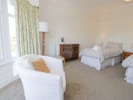 A bedroom with twin beds a white armchair a wooden cabinet a floor lamp and green floral curtains at Seawinds 2a in Rhos-On-Sea