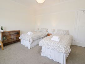 A bedroom with two single beds a wooden shelf with books and a plant and a closed white door at Seawinds 2a in Rhos On Sea