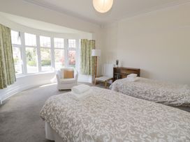 A bedroom with two single beds and a white armchair in front of a large bay window at Seawinds 2a in Rhos-On-Sea