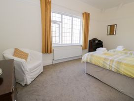A bedroom with two single beds with folded towels a white armchair a wooden dresser and a window with yellow curtains at Seawinds 2a in Rhos-On-Sea