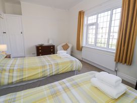 A bedroom with two single beds with yellow plaid bedding and white towels a wooden chest of drawers a white chair with a cushion and a window with yellow curtains at Seawinds 2a in Rhos-On-Sea