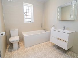 A bathroom with a toilet bathtub wall-mounted sink and illuminated mirror at Seawinds 2a in Rhos-On-Sea