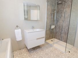 A bathroom with a shower enclosure a white sink cabinet a wall mirror and a towel hanging at Seawinds 2a in Rhos-On-Sea
